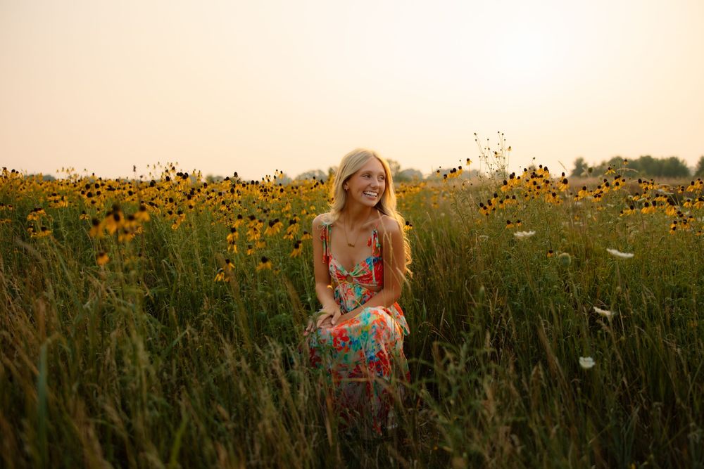 A person in a floral dress walks through a vibrant field of wildflowers during golden hour.