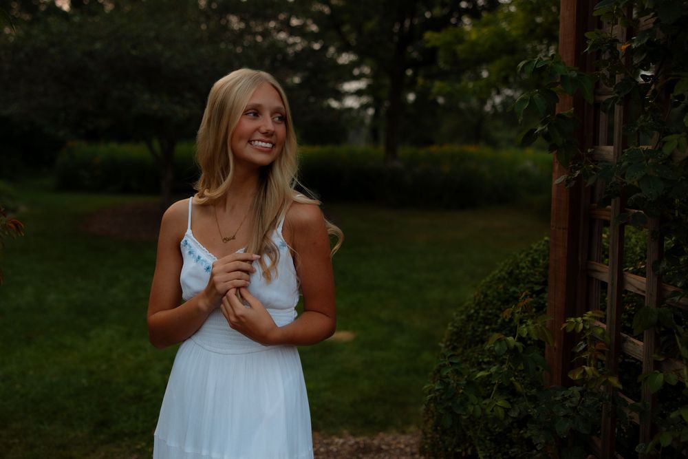 A person in a white summer dress stands in a lush garden setting during golden hour lighting.