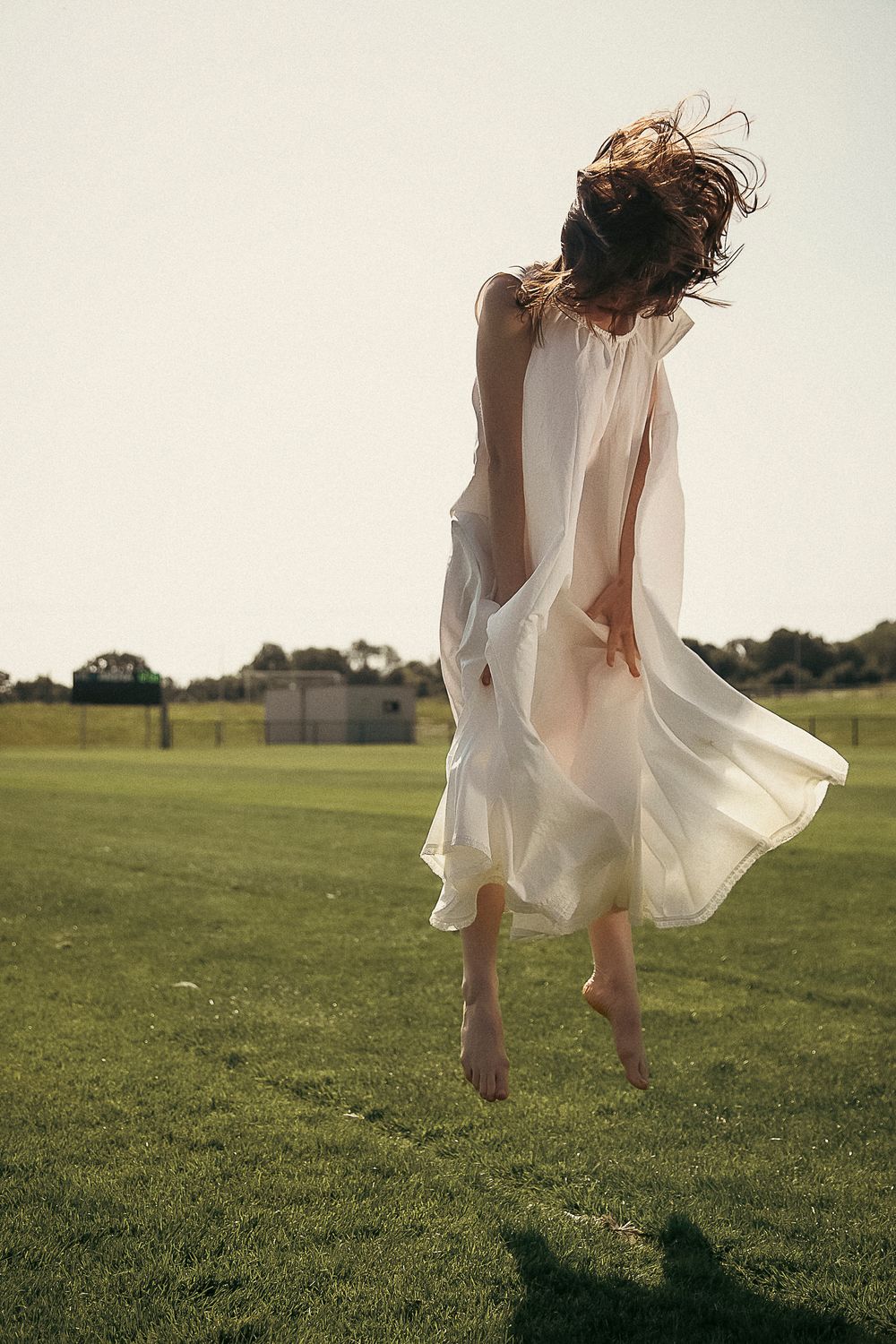 A dreamy sequence of a figure in a flowing white dress jumping and twirling across a sunlit grassy field.
