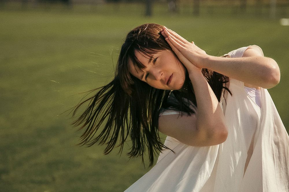 A person in a white dress twirls gracefully in a sunlit meadow with long flowing hair.