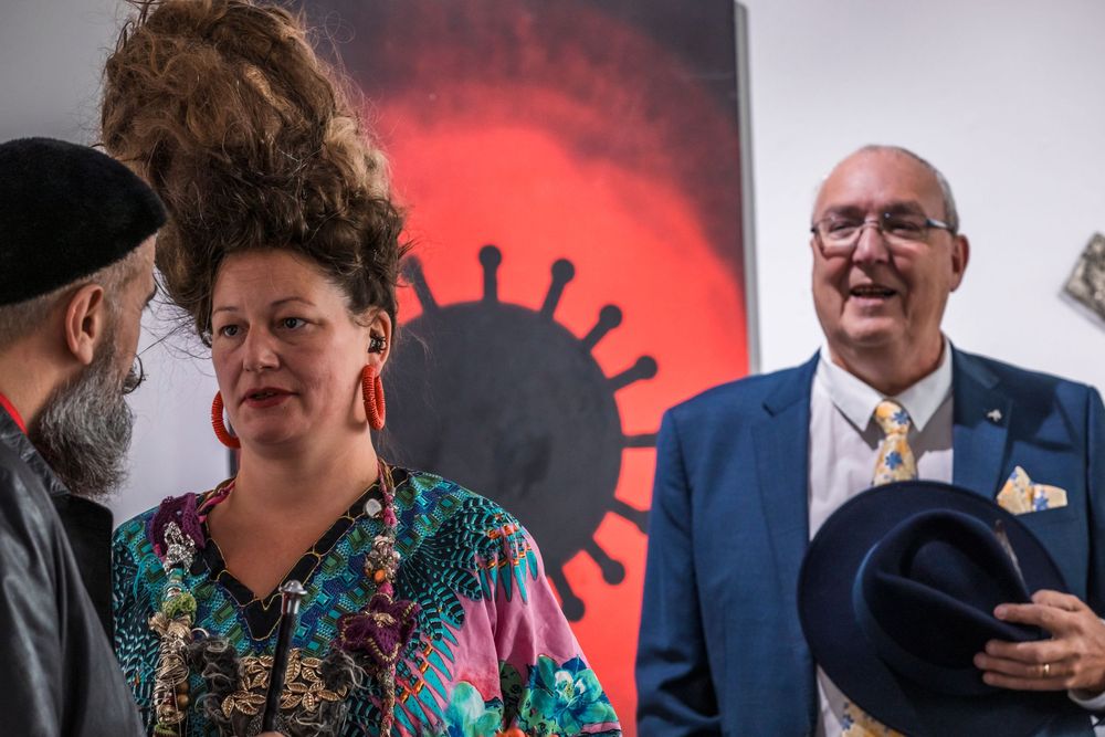 Three people stand and chat at an event with a red circular design visible on the wall behind them.