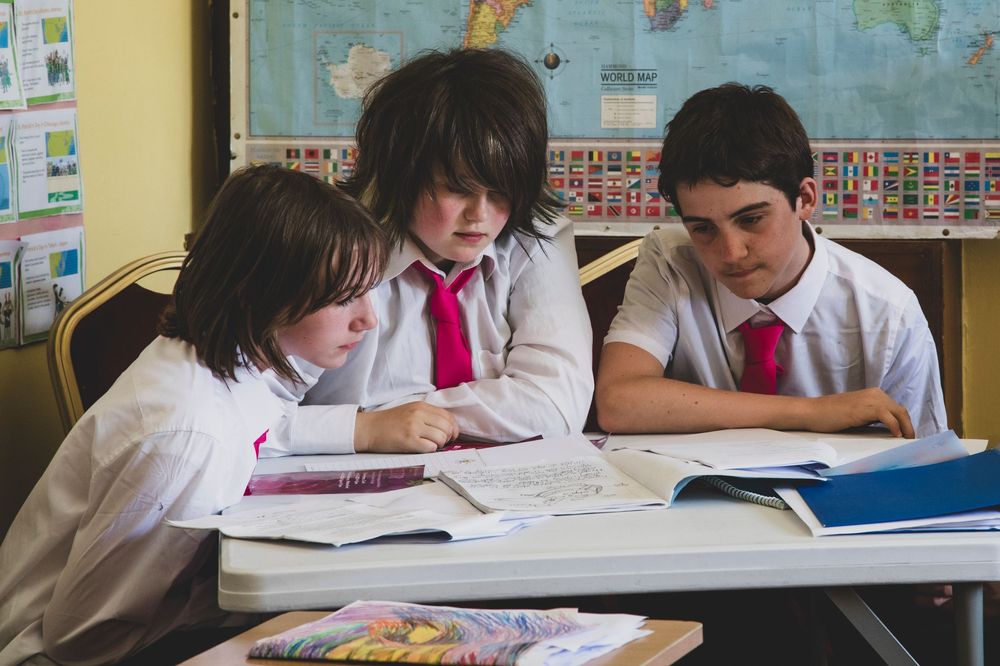Students work diligently at desks in a classroom with a colorful world map displayed on the wall.
