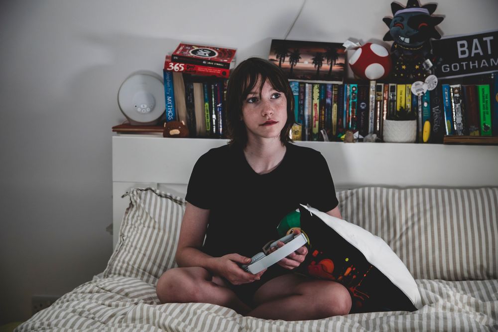 A person sitting on a couch in a dimly lit room with bookshelves and decorations visible in the background.