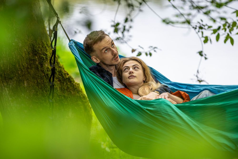 Couple relaxing together in a colorful hammock outdoors, surrounded by lush green trees.