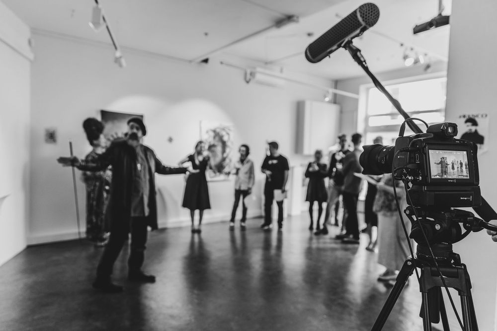 Behind the scenes of a film production with camera crew and talent in a white studio space.