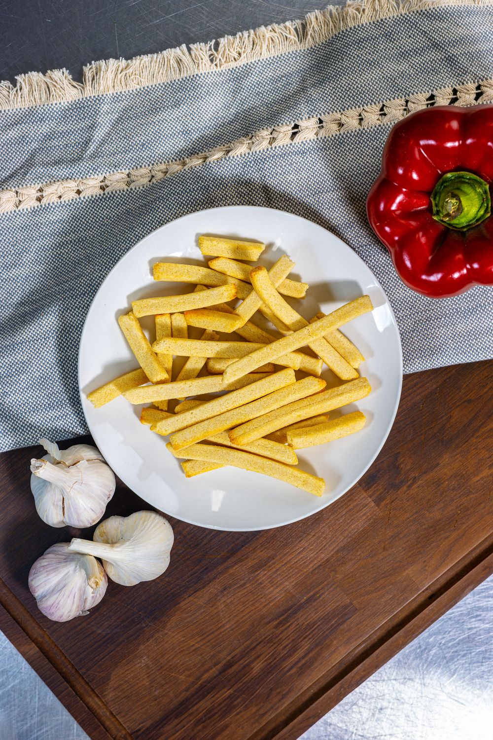 A series of photos showing raw polenta fries arranged on white plates with garlic and red peppers on a wooden cutting board.