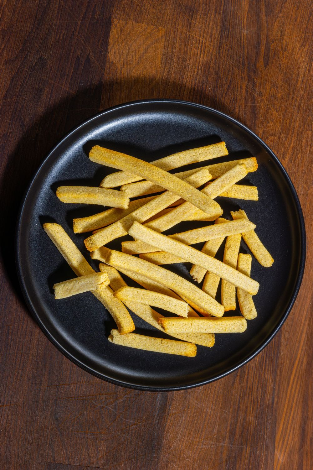 Golden french fries arranged in neat rows on a black plate against a dark wooden surface.