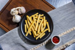 Golden french fries served in a black plate on a wooden board with garlic and red dipping sauce.