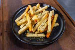 Crispy golden french fries with fresh herbs served on black plates against a rustic wooden table surface.