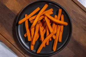 Sweet potato fries arranged on a black plate against a rustic wooden background, showing cooking progression.