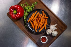 Fresh vegetables including red peppers, carrots, garlic, and herbs arranged on wooden cutting boards against dark background.