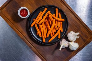 Fresh carrots being sliced into thin strips on a wooden cutting board with garlic cloves nearby.