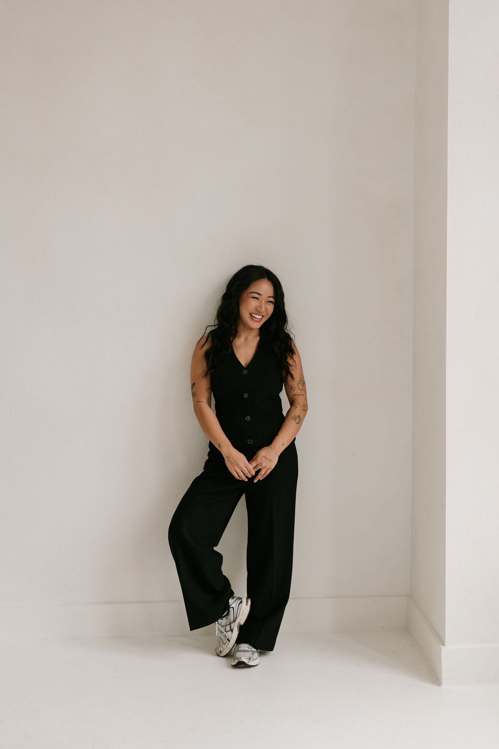 A person in a black jumpsuit poses playfully against a white studio backdrop in a series of candid shots.