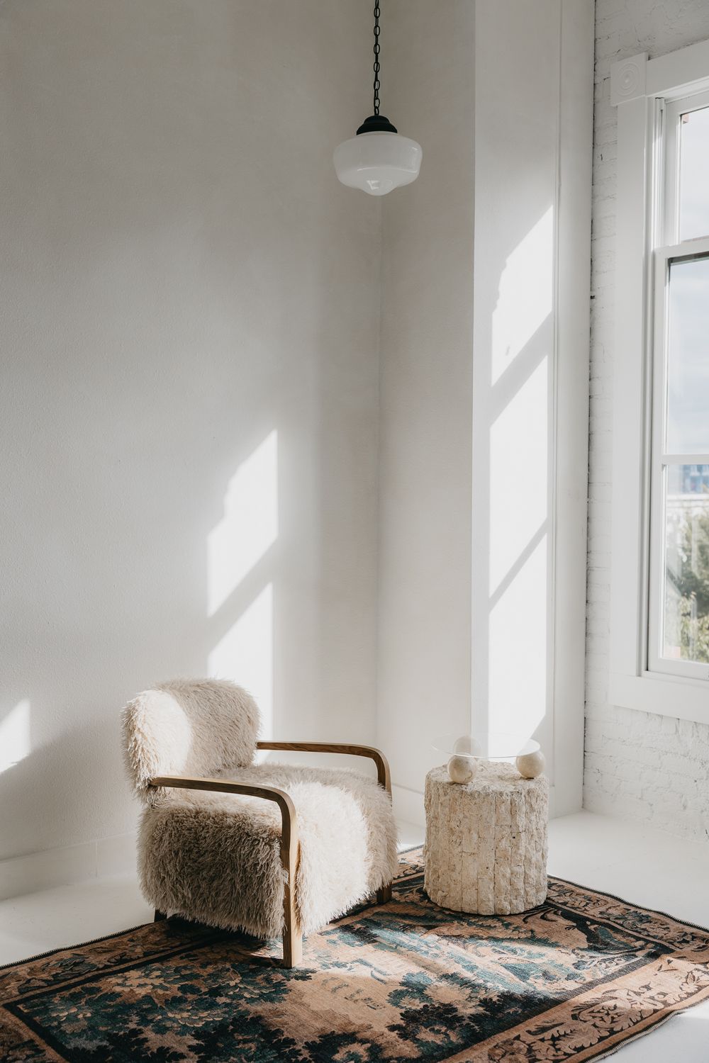 Minimalist white room interior with vintage rug and plush seating by sunlit windows casting dramatic shadows.