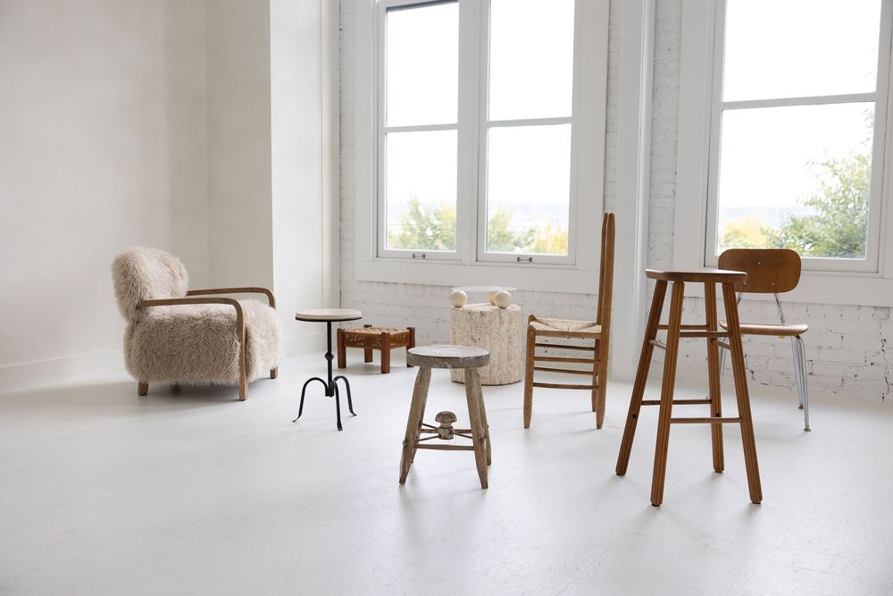 Minimalist white interior design space with wooden chairs and large windows letting in natural light.