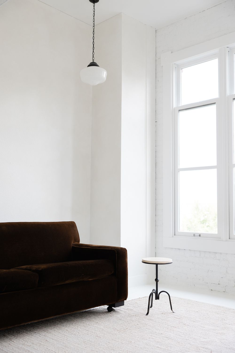 Minimalist white room interior with dark brown sofa and floor lamp against bright windows and white walls.