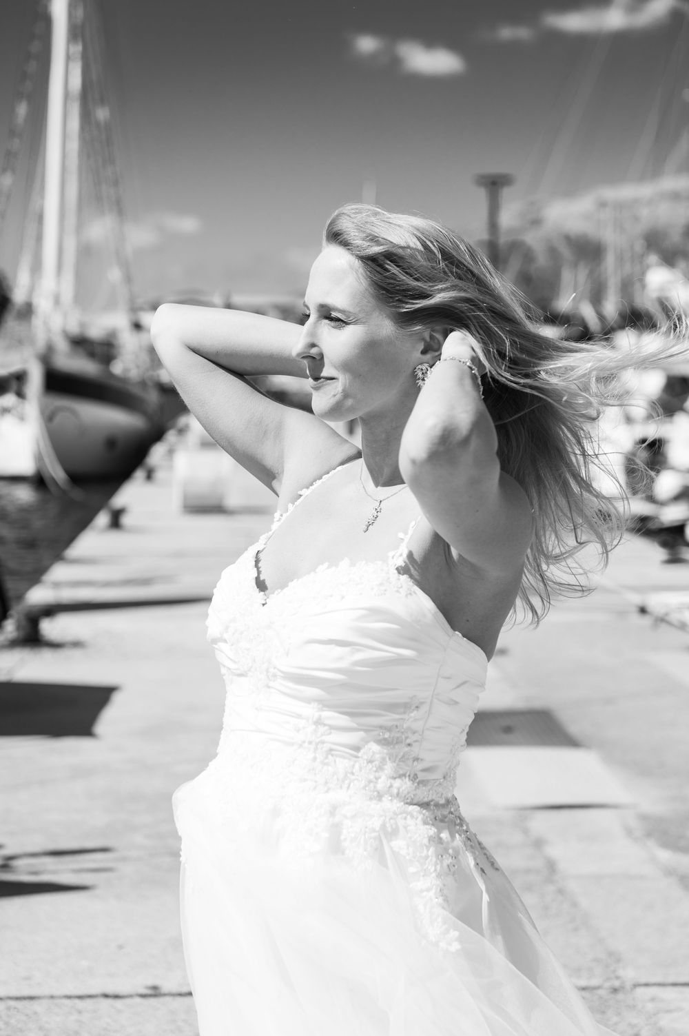 A flowing white dress twirls gracefully against a bright outdoor backdrop at a marina.