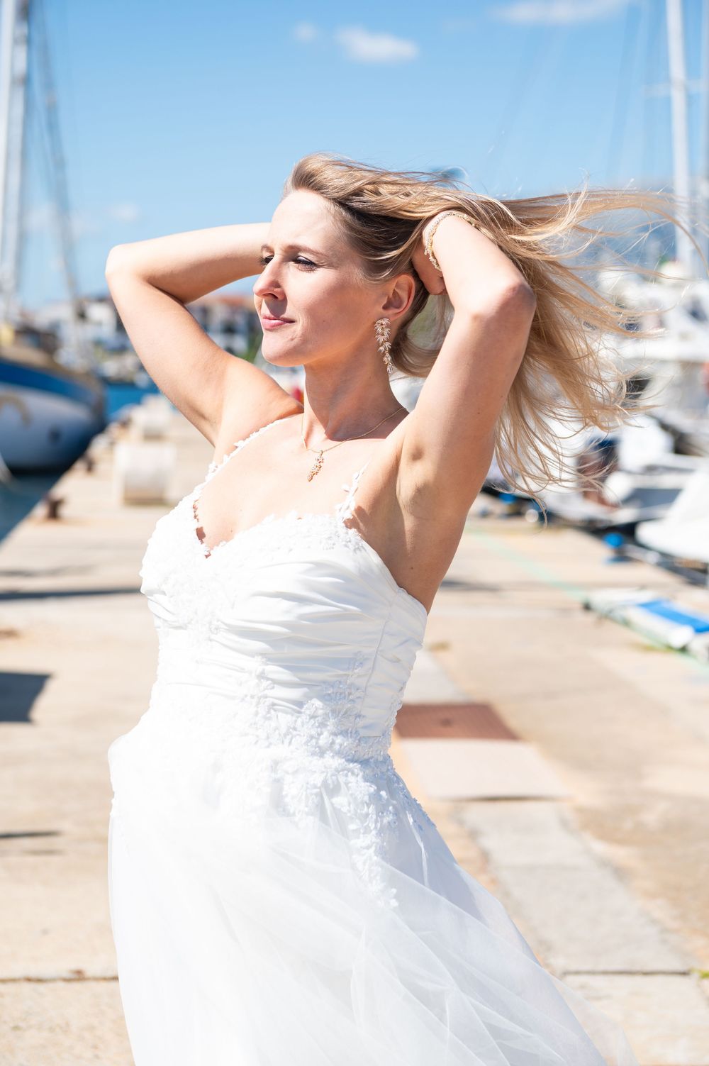 A white sundress flows in the breeze at a sunny marina with boats in the background.
