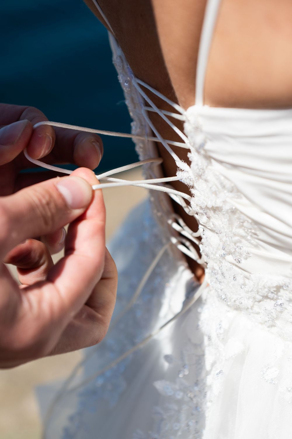Close-up detail of white dress lacing being adjusted.