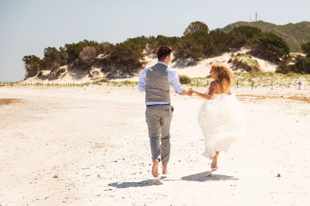 A couple walking along a pristine white sandy beach with turquoise waters in the background.