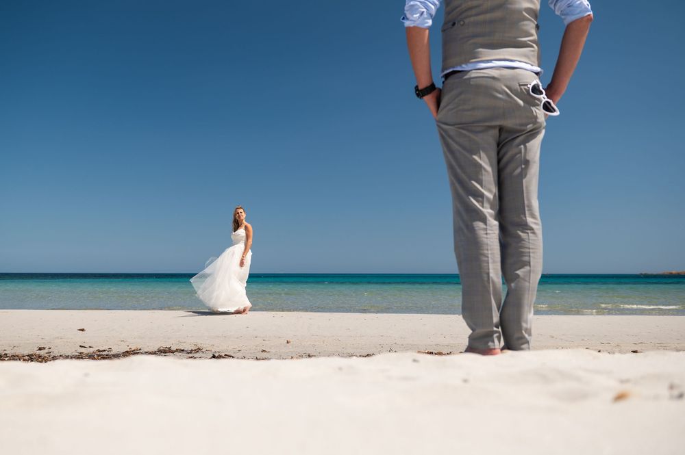 Wedding couple poses on a scenic beach with crystal clear turquoise waters in the background.