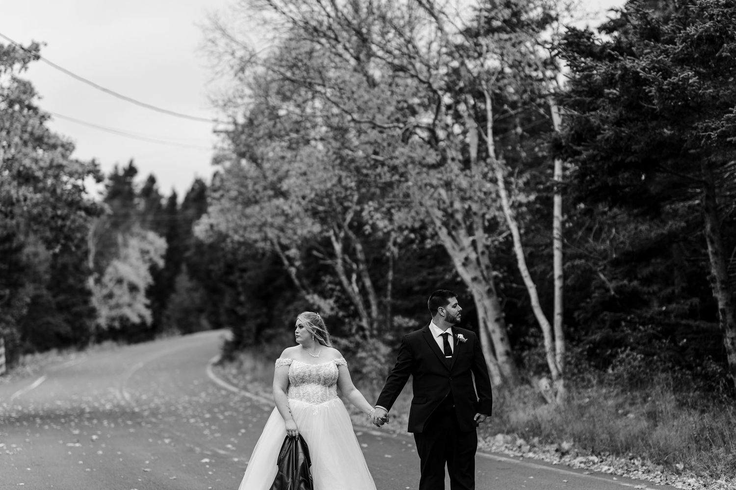 A couple walks down a tree-lined country road on a sunny day in black and white photography.