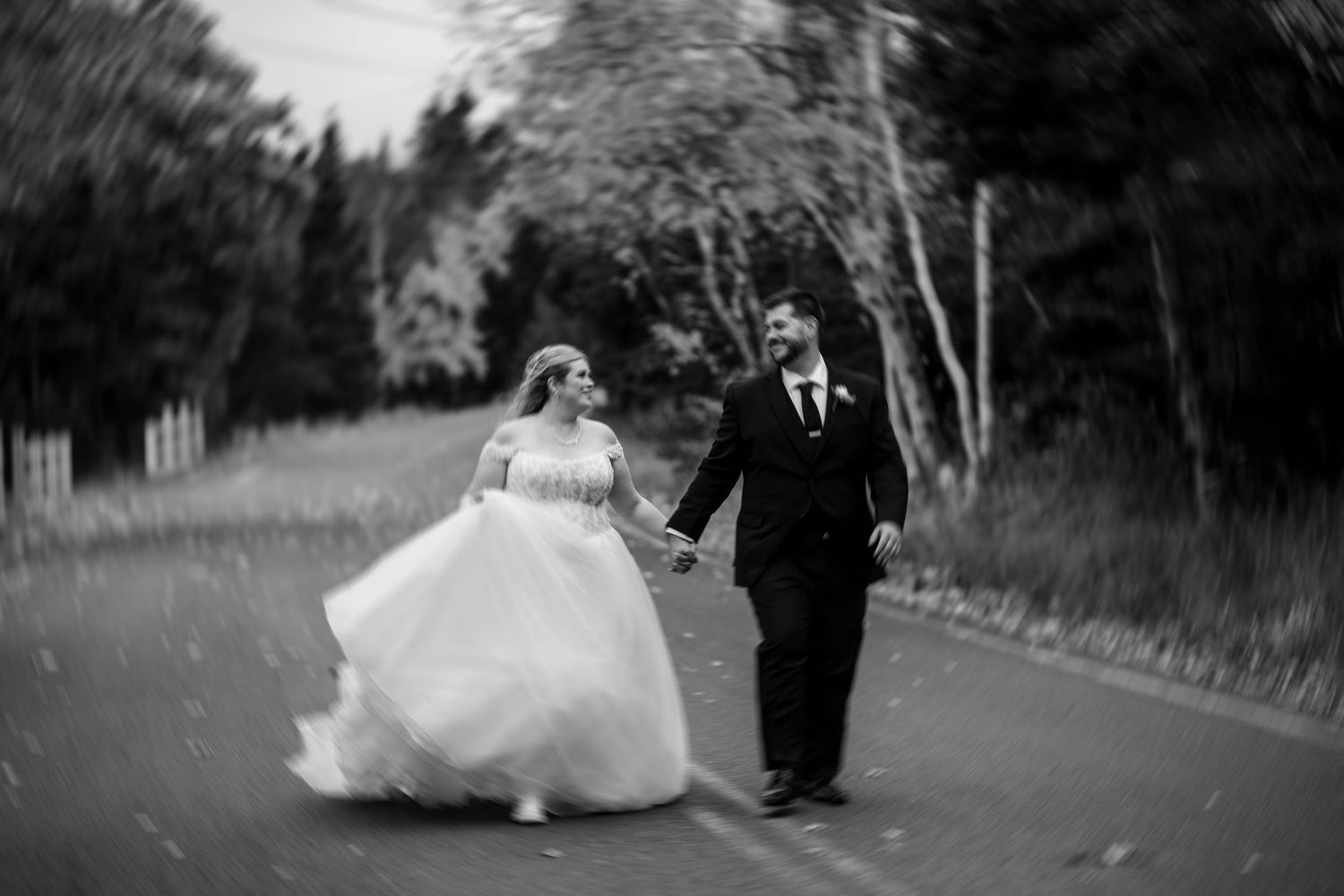 Black and white wedding photos show a couple walking and dancing together on a tree-lined path outdoors.