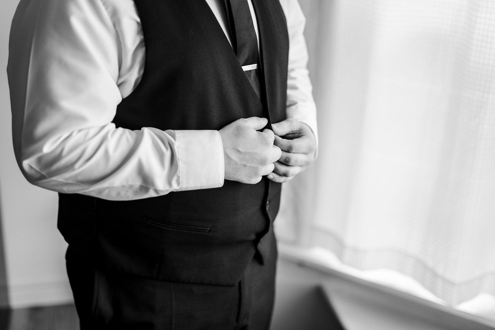 Black and white close-up of someone adjusting their formal black vest over a white dress shirt.