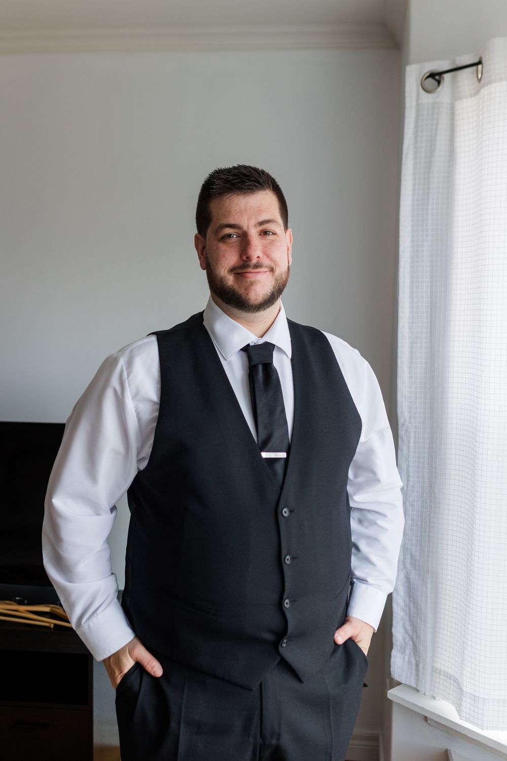 Professional formal attire with black vest and white dress shirt shown in multiple poses near a window.