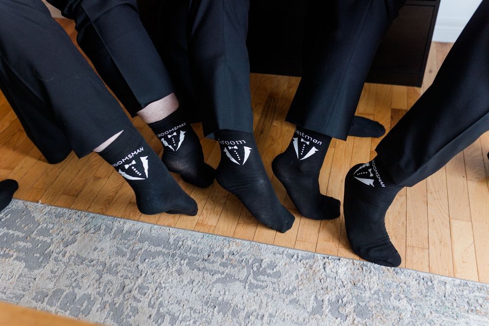 Legs and feet of people wearing formal black shoes and pants lined up on a hardwood floor.