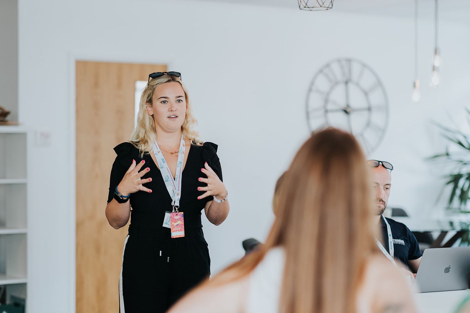 Professional speaker gestures while giving a business presentation to an audience in a bright modern office space.