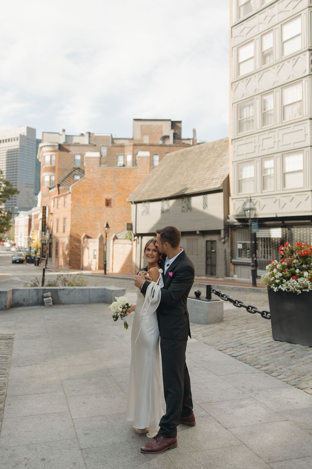 Newlyweds dancing together on cobblestone street surrounded by historic brick buildings.