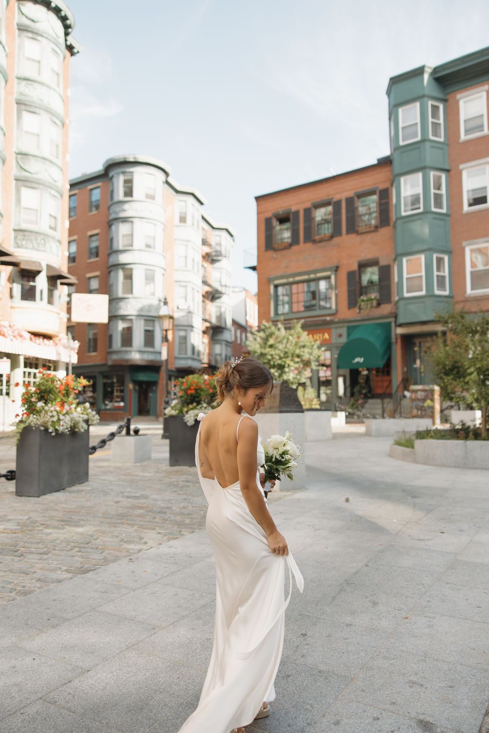 Bride in flowing white dress walking through historic urban neighborhood.