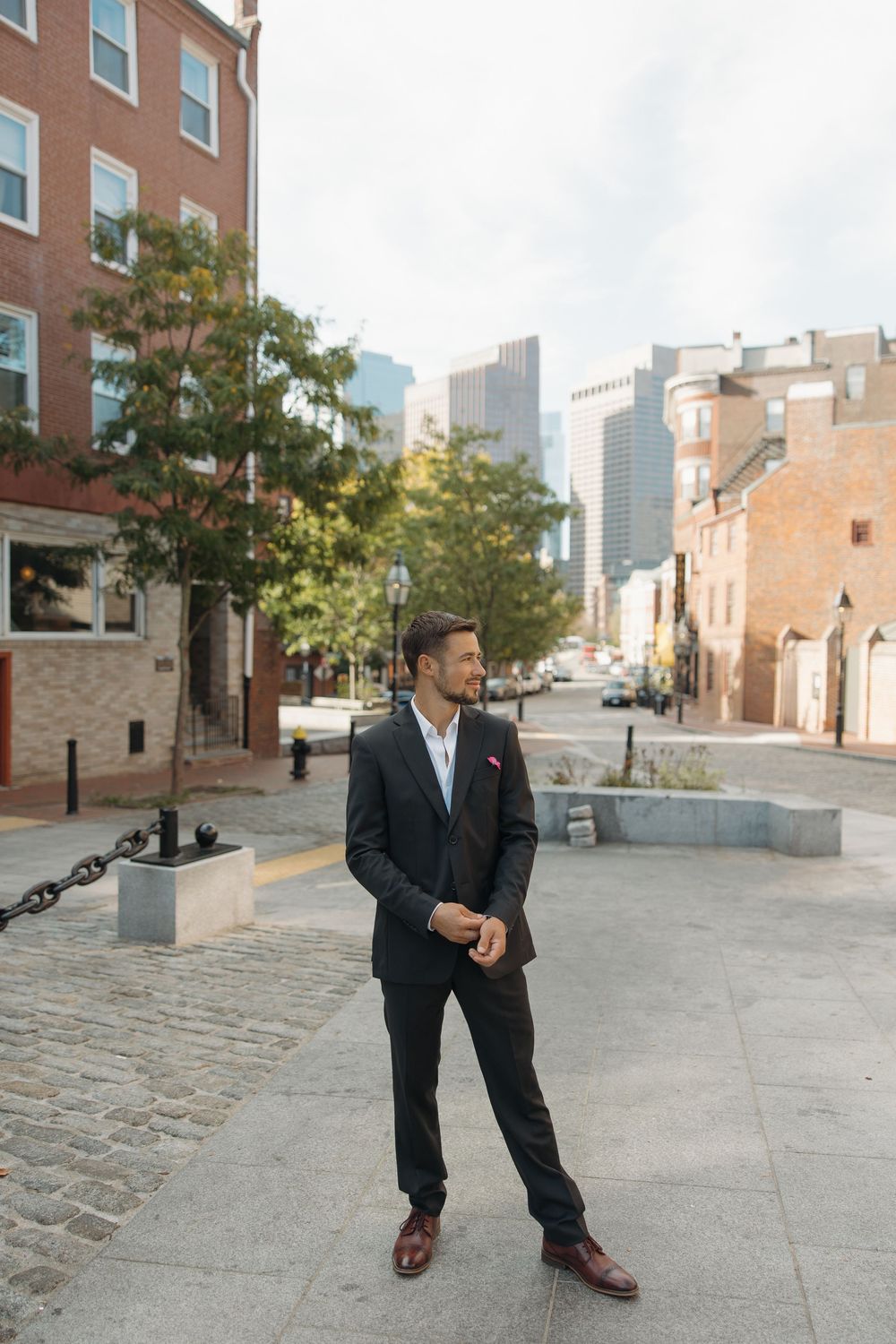 Candid shots of groom on cobblestone street with city buildings in background.