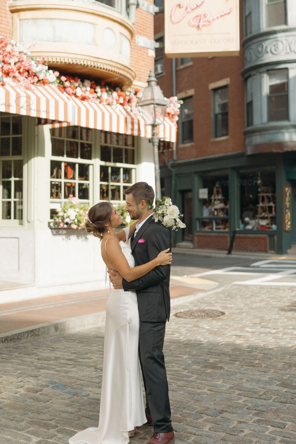 Wedding couple shares first dance on cobblestone street near vintage storefront.