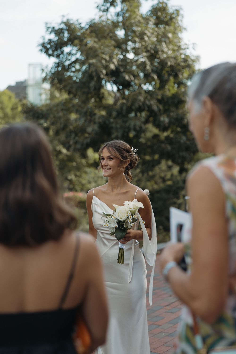 Wedding party gathered outdoors on a sunny day with trees in the background.