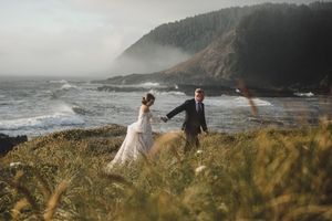 Couple walking along rugged coastline with mountains and ocean views on foggy afternoon.