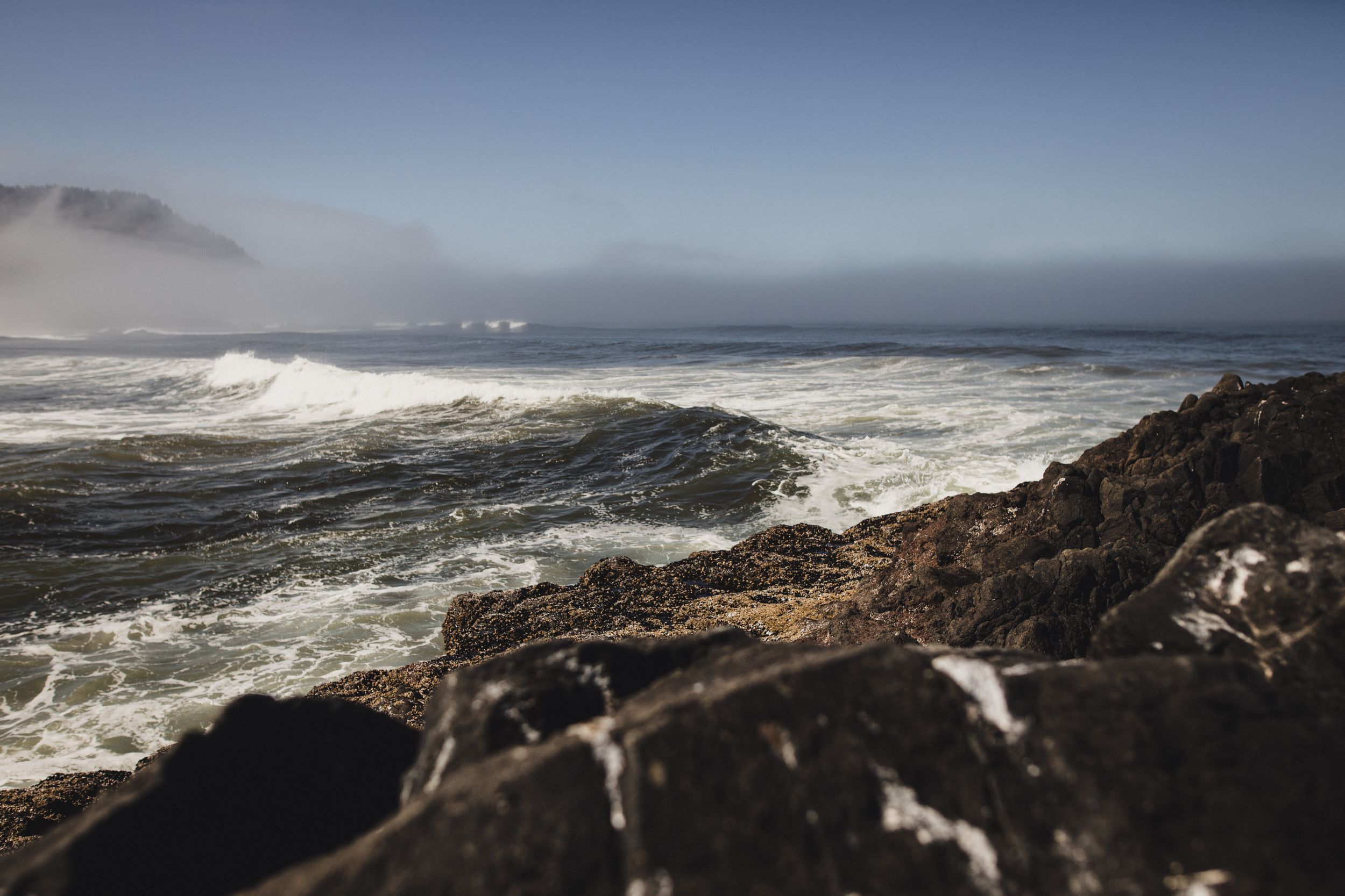 Panoramic view of rugged coastal cliffs with crashing ocean waves against rocky shoreline during stormy weather.