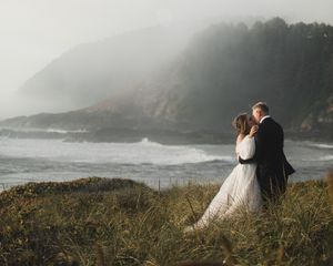 Misty coastal landscape with couple embracing on grassy cliff overlooking the ocean.