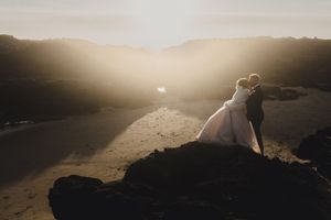 Silhouetted couple embraces on a hilltop during golden hour with dramatic sunlit clouds in the background.