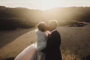 Silhouetted couple embracing on a beach at golden hour with dramatic coastal cliffs in the background.