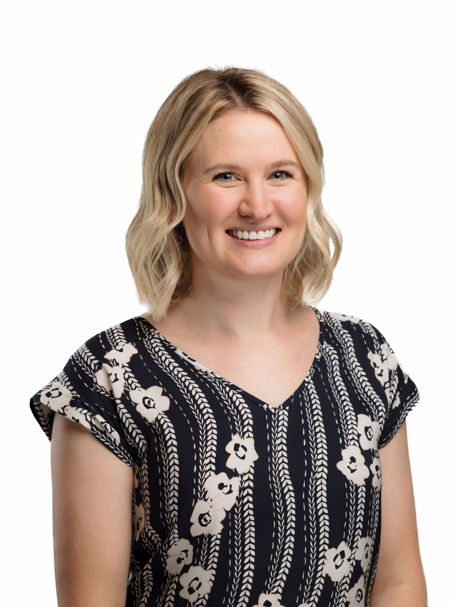 Professional headshot of someone wearing a black and white patterned short-sleeve top against a white background.