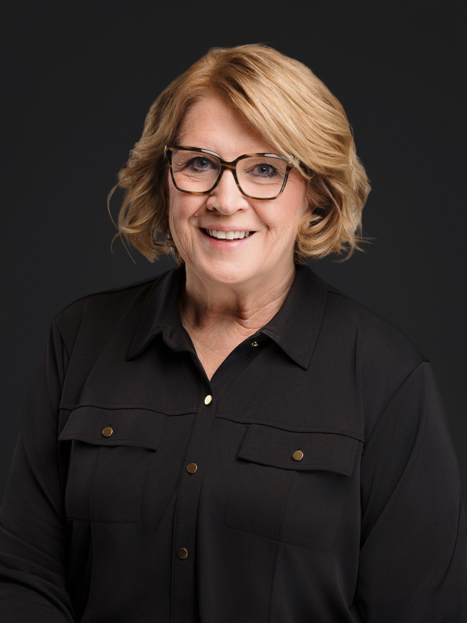 Professional portrait series showing person in black button-up shirt and glasses against dark background with warm lighting.