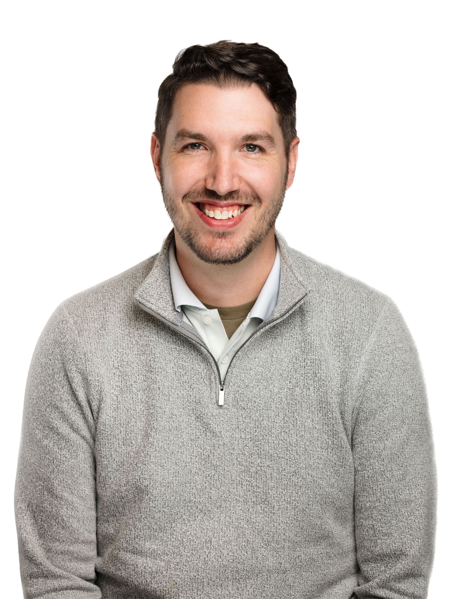A person wearing a grey quarter-zip sweater smiles warmly against a white background in a professional headshot.