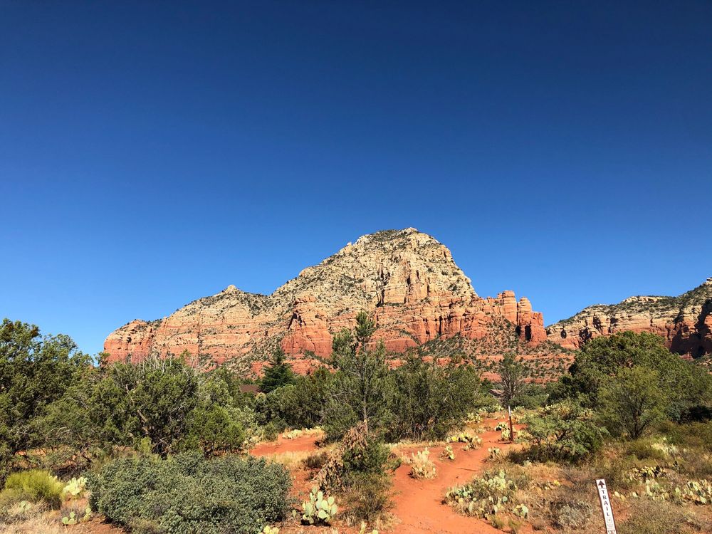 Panoramic view of red rock formations and desert landscape in Sedona against bright blue sky.