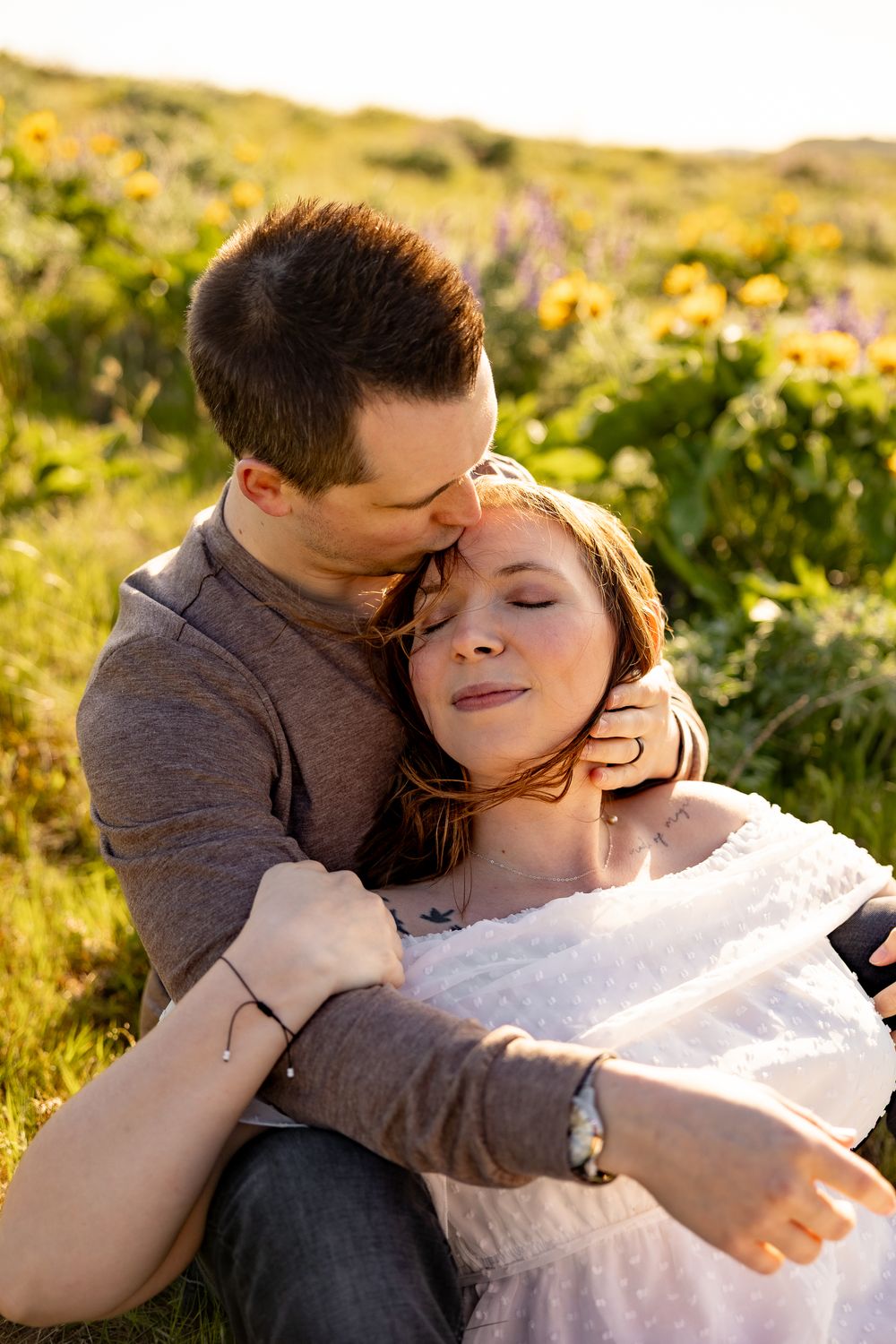 An intimate moment shared between a couple among blooming wildflowers on a sunny hillside.