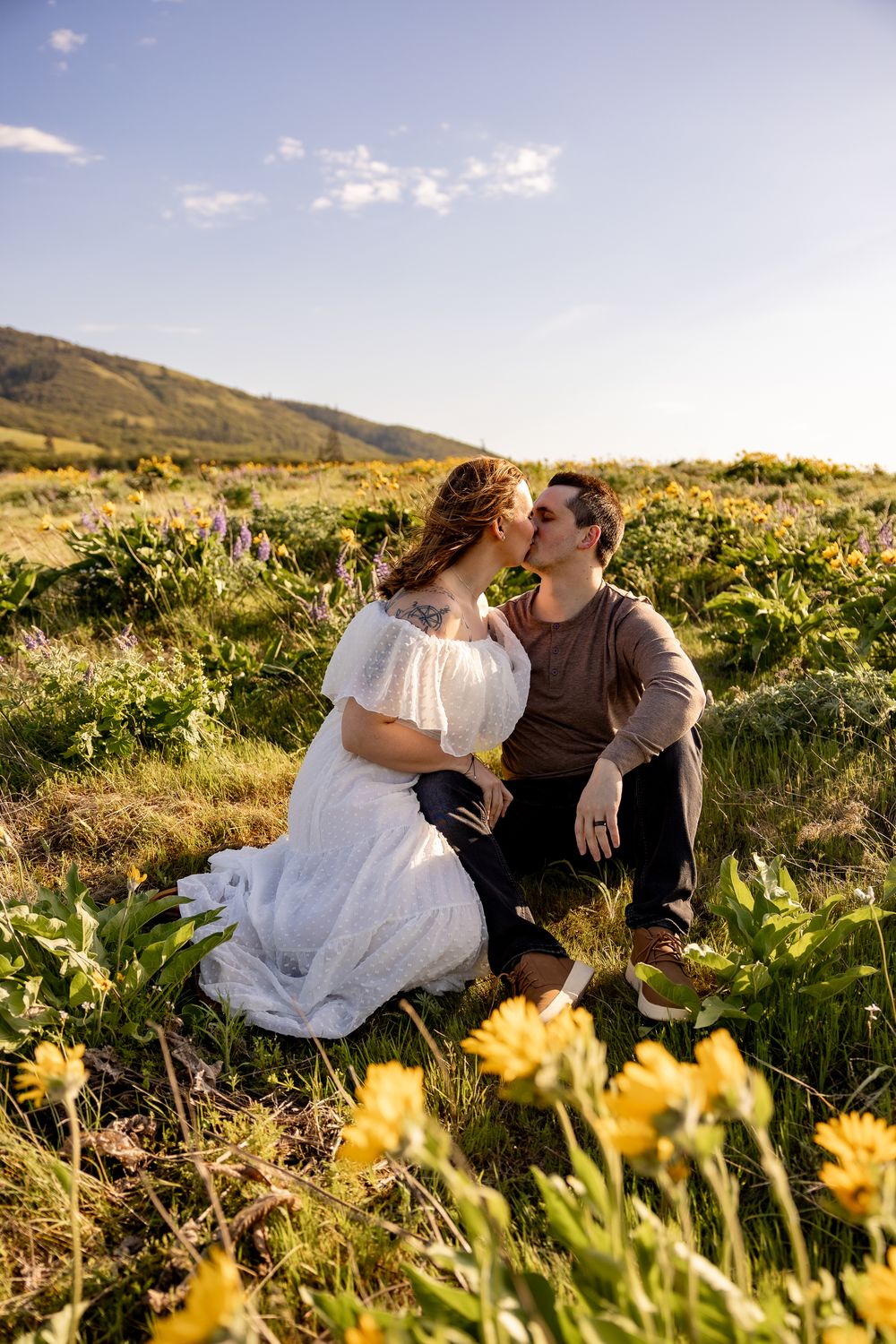 A romantic moment shared in a field of yellow wildflowers with mountains in the background.