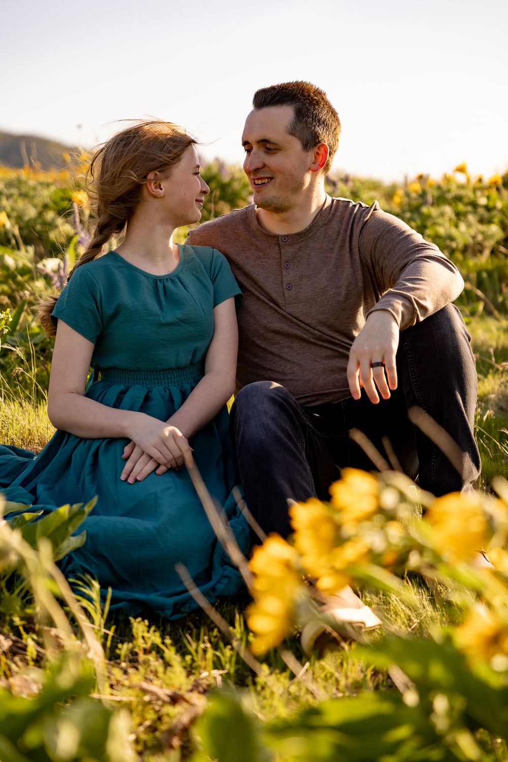 A couple shares a loving moment while sitting in a field of yellow flowers at sunset.