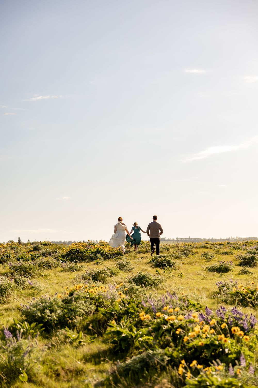 People walking through a scenic mountain meadow filled with wildflowers at sunset.