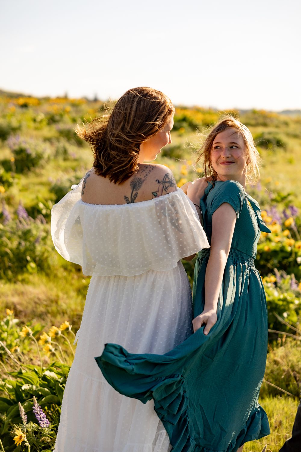 Two people in teal and white dresses dance together in a sunny mountain meadow.